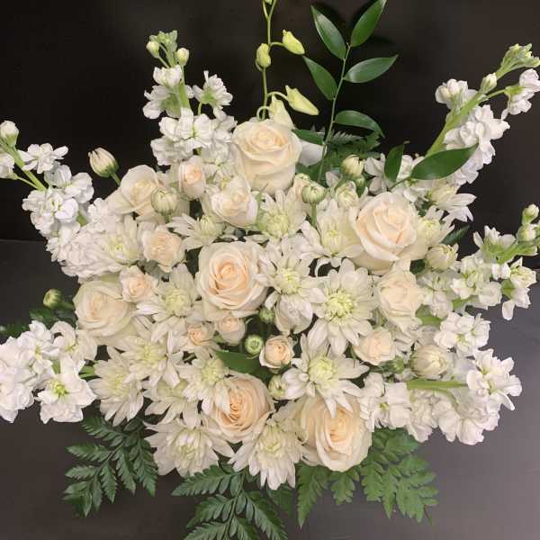 Cream roses and white flowers arranged in a low bouquet against a dark background.