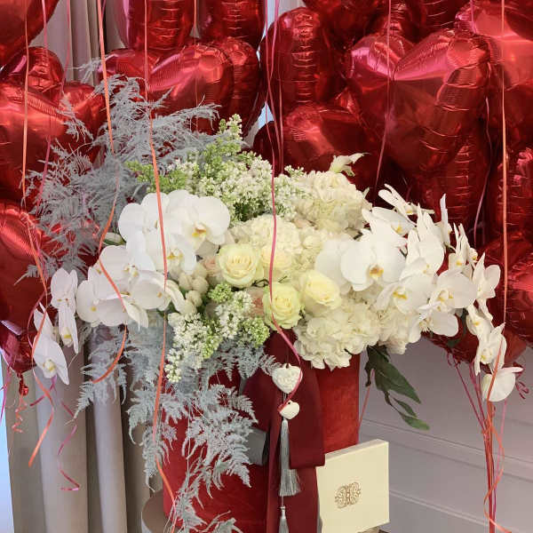 White floral arrangement with red heart balloons and ribbon streamers