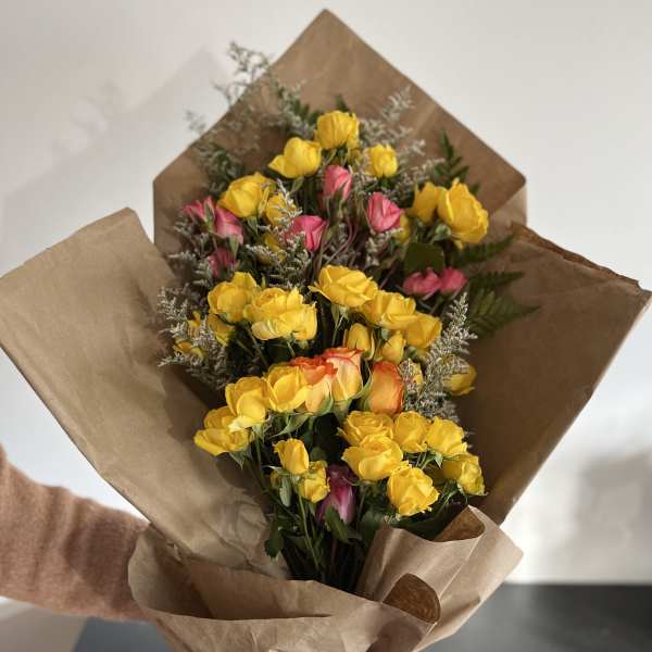 Bouquet of yellow and pink roses wrapped in brown paper with a pink ribbon