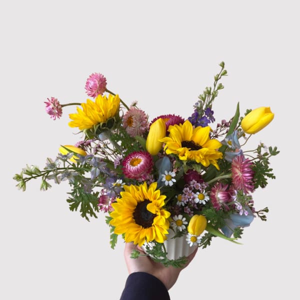 Bouquet of sunflowers, tulips, and small mixed blooms in a white vase