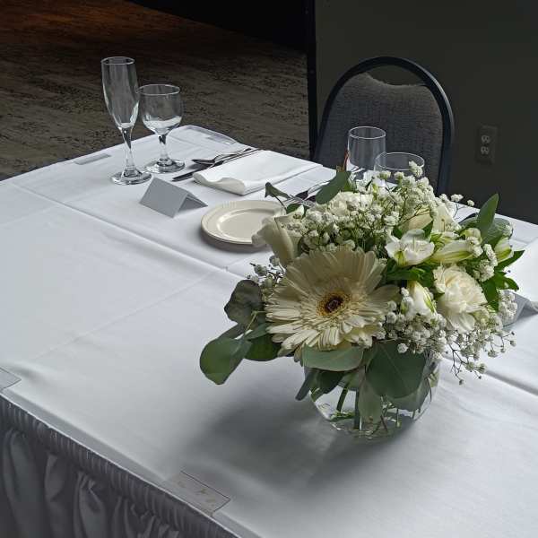 White floral centerpiece in a clear glass vase on a set dining table