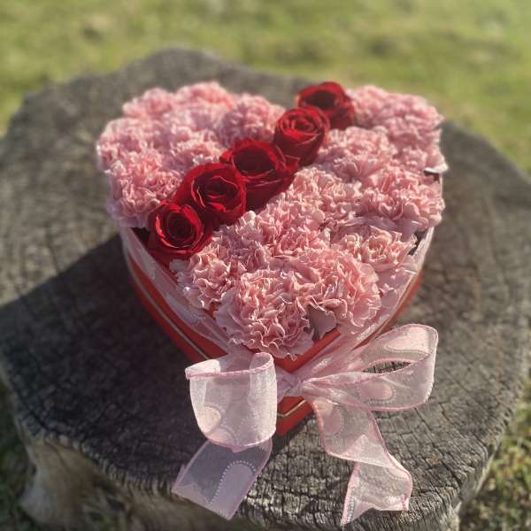 Heart-shaped box of pink carnations with red roses and a pink ribbon