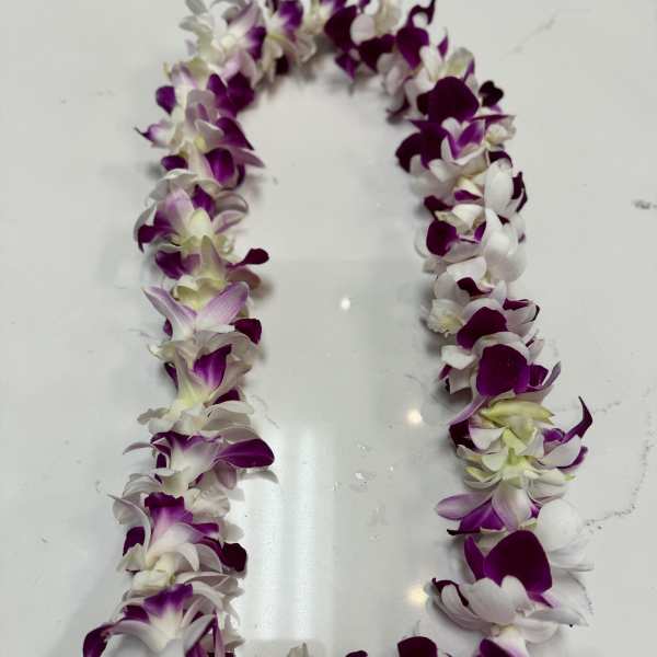 Purple and white orchid lei laid in a loop on a white surface