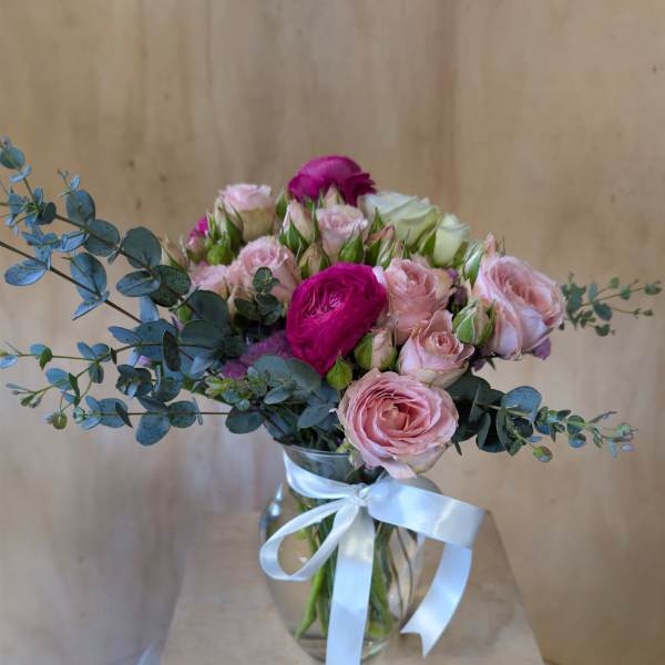 Pink roses and ranunculus in a glass vase with a white ribbon