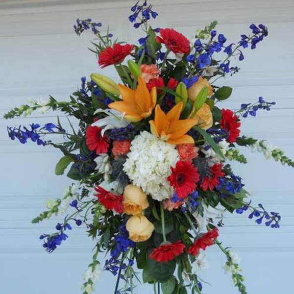 Tall mixed floral spray with orange lilies, red daisies, and blue flowers on an easel