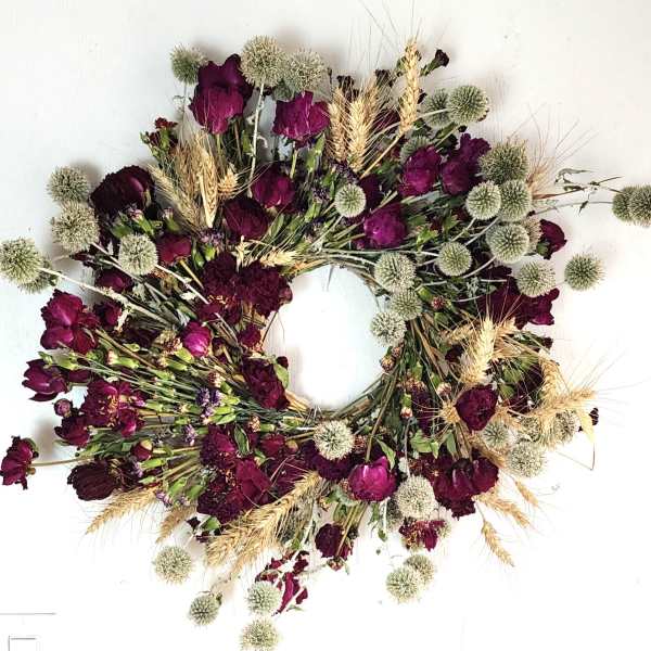 Circular wreath of burgundy flowers and pale seed heads on a white background
