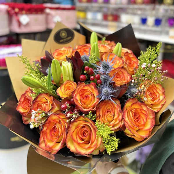 Hand-tied bouquet of orange roses with lilies and accent flowers in decorative wrap