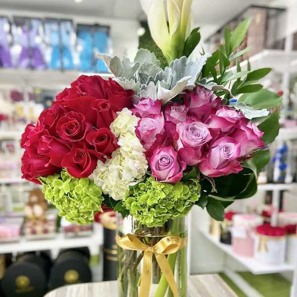 Tall glass vase with red and pink roses, green hydrangeas, and white calla lilies.