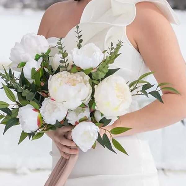 Bride holding a white peony bouquet with greenery and a trailing blush ribbon