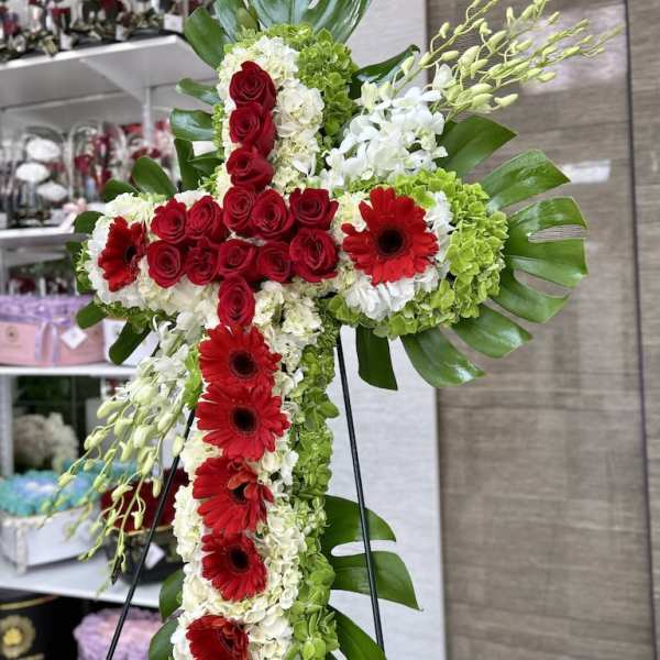 Standing cross-shaped arrangement of red roses and gerberas with white and green blooms on a metal easel.