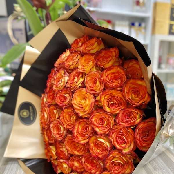 Large bouquet of tightly packed orange and yellow roses wrapped in tan and black paper