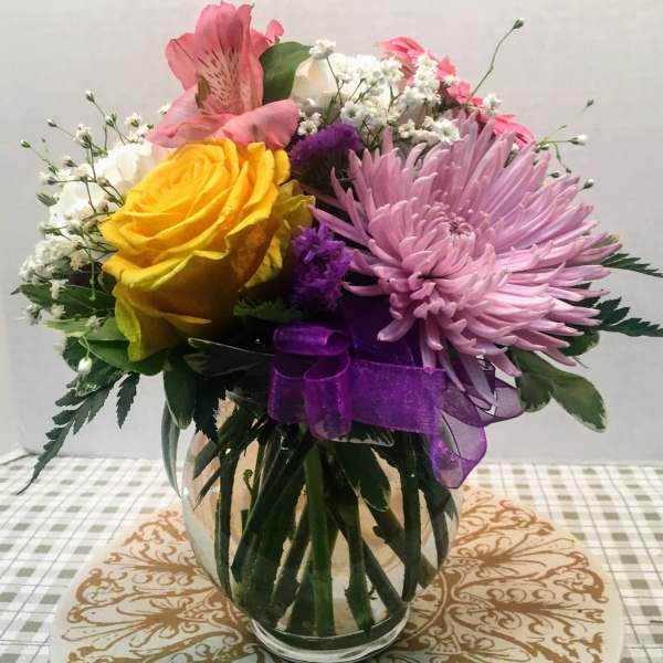 Bouquet of yellow and pink flowers in a glass vase with a purple ribbon