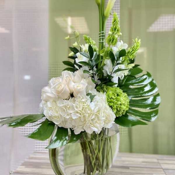 Tall white calla lilies with white roses and hydrangeas in a clear glass vase.