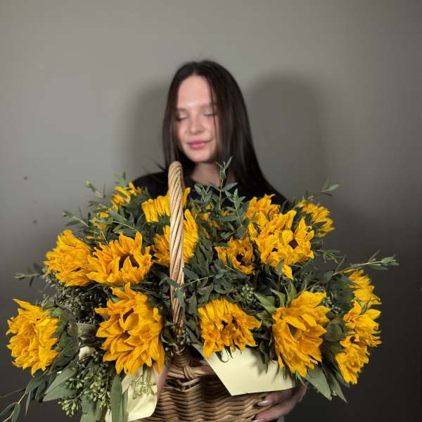 Basket of bright yellow sunflowers held by a woman