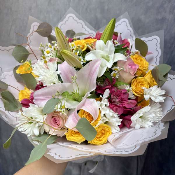 Handheld bouquet of pink lilies, yellow roses, and white daisies