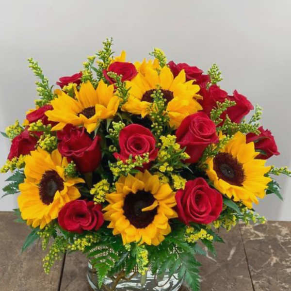 Bouquet of red roses and yellow sunflowers in a clear glass vase