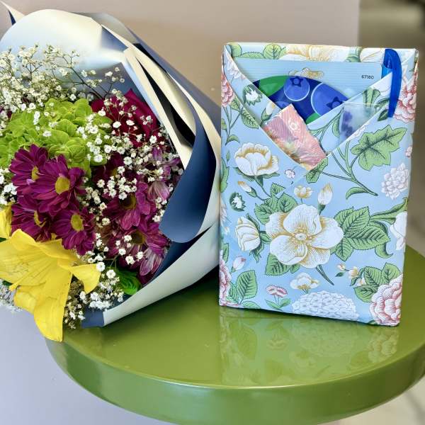 Bouquet of purple and yellow flowers beside a floral-print gift pouch on a green table