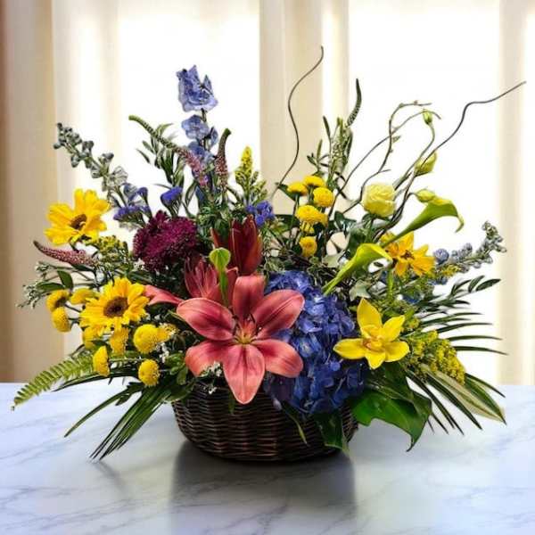 Mixed flower arrangement in a wicker basket with lilies and sunflowers