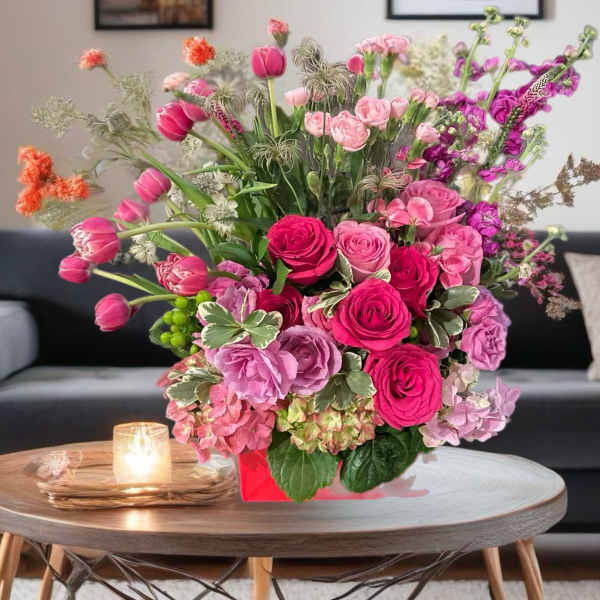 Pink and purple mixed flower arrangement in a red box on a table