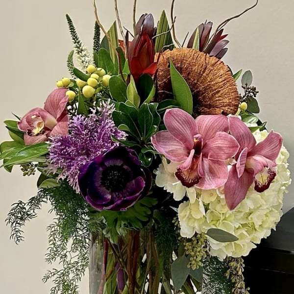Tall mixed floral arrangement in a clear glass vase with orchids and hydrangea