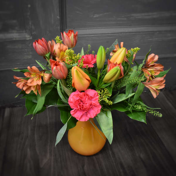 Bouquet of orange tulips, pink carnations, and alstroemeria in a yellow vase