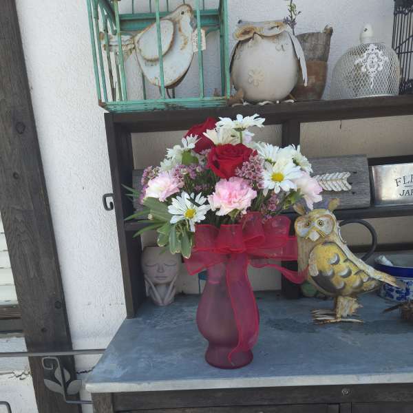 Bouquet of red roses, white daisies, and pink carnations in a frosted vase with a red ribbon