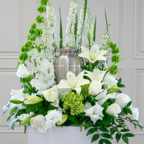 White lilies and roses arranged around a silver urn with green accents
