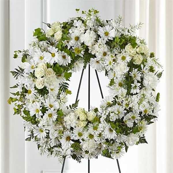 White floral wreath on a black stand with daisies and roses
