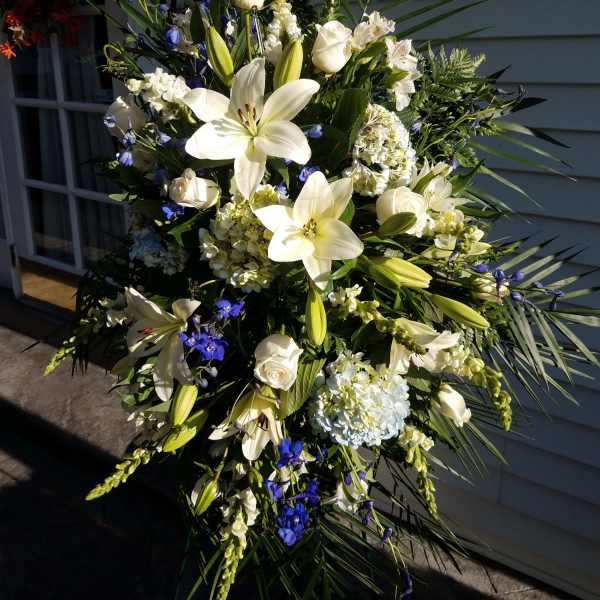Tall white floral spray with lilies, roses, and blue accents