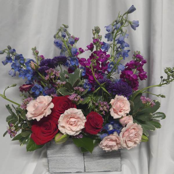 Mixed bouquet of red and blush roses with blue and purple flowers in a wooden box