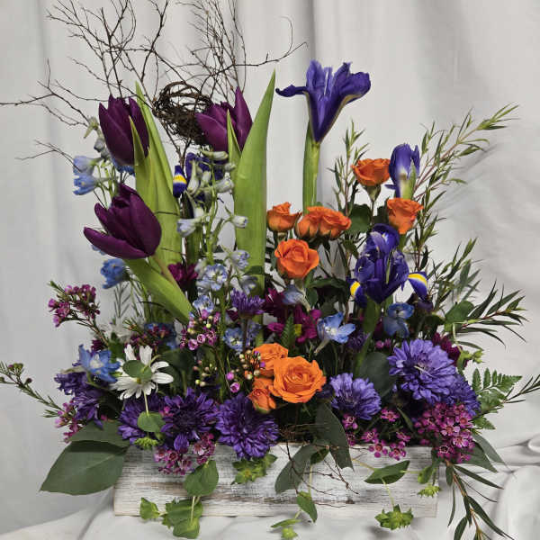 Purple tulips, orange roses, and blue irises in a white wooden box