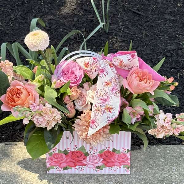 Pink and peach flower arrangement in a decorative gift bag with a floral ribbon