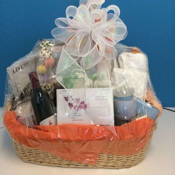 Gift basket with orchids, wine, a candle, and assorted items wrapped in cellophane