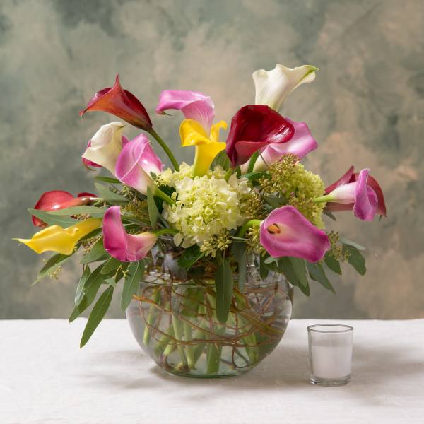 Mixed calla lily bouquet in a glass bowl vase with a small candle beside it