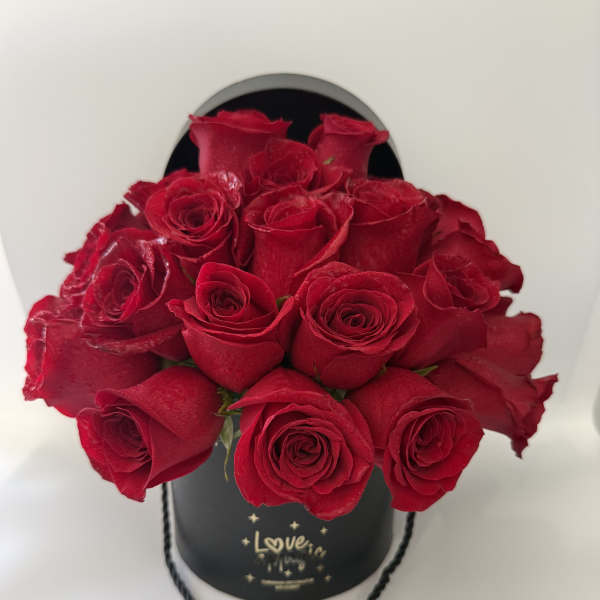 Red roses arranged in a black hatbox with a rope handle