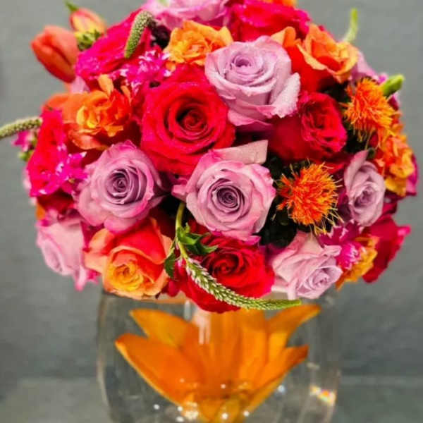 Mixed bouquet of roses and orange blooms in a clear glass vase