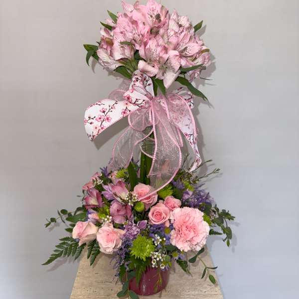 Pink floral arrangement with a butterfly topper and ribbon in a vase