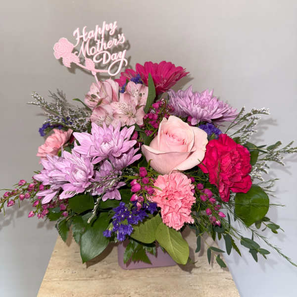 Pink and lavender mixed bouquet with a Mother's Day topper in a square vase