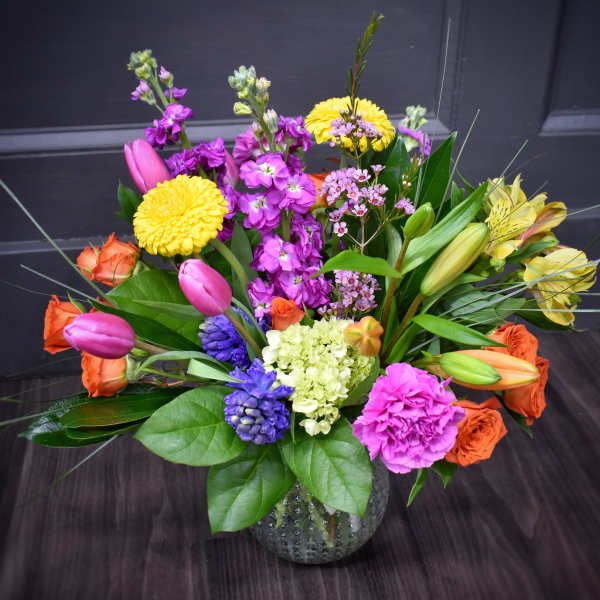 Colorful mixed bouquet in a glass vase with tulips, roses, lilies, and mums