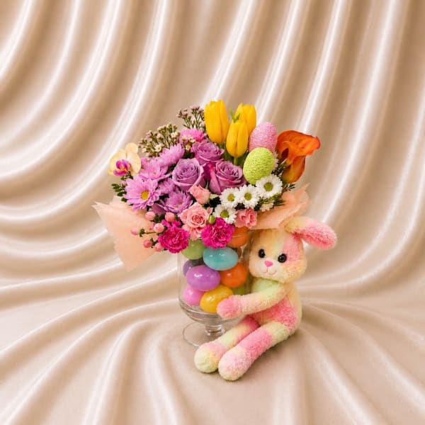 Colorful bouquet in a glass vase with a plush bunny beside it
