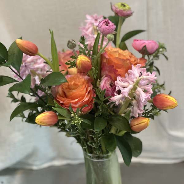 Mixed bouquet with orange roses, pink tulips, and pale pink blooms in a glass vase