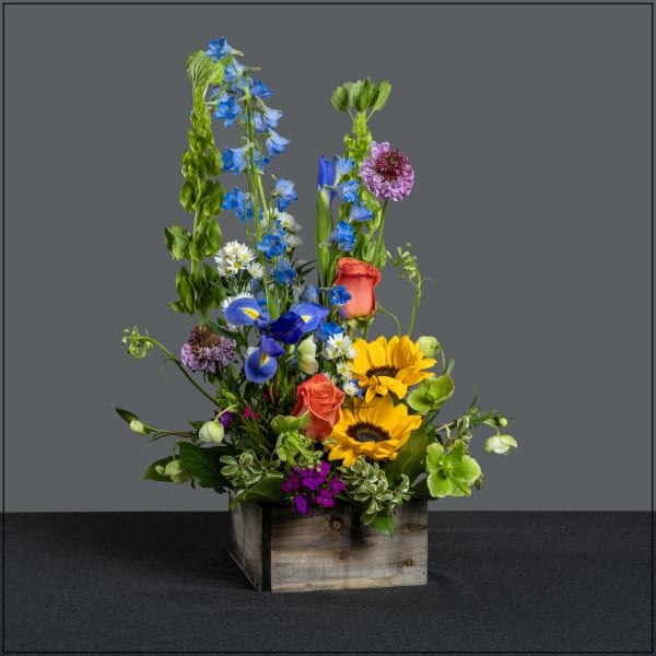 Mixed bouquet in a wooden box with sunflowers, blue irises, and roses