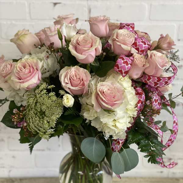 Pink roses and white blooms arranged in a glass vase with heart ribbon