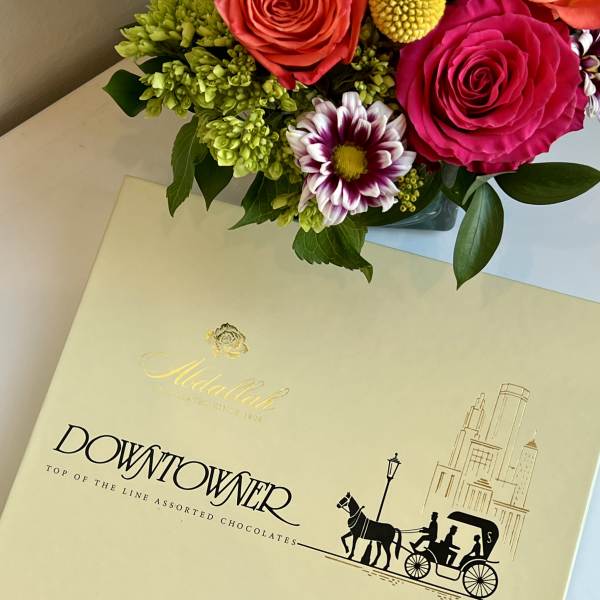 Box of assorted chocolates with a small floral arrangement on top