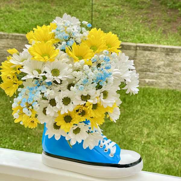 Bouquet of yellow and white daisies with blue baby's breath in a blue sneaker vase
