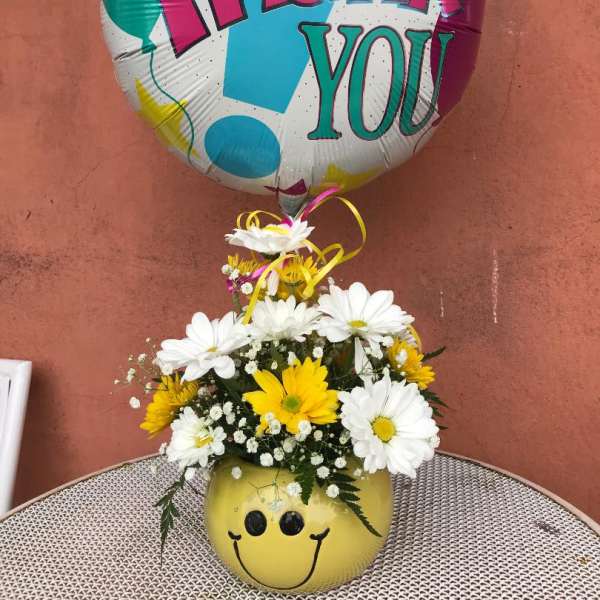 Daisy bouquet in a smiley-face vase with a colorful thank-you balloon