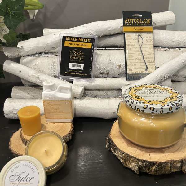 Assorted candles and fragrance products arranged on wood slices with white birch logs.