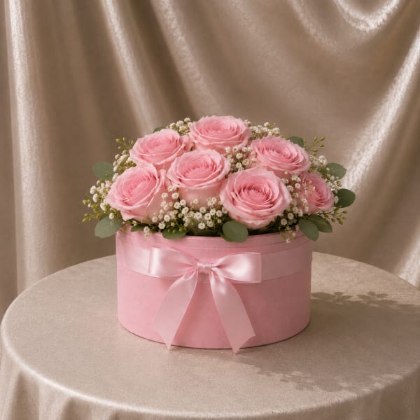 Pink roses arranged in a round pink box with a satin bow