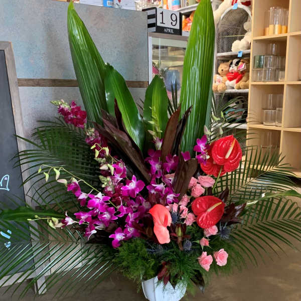 Tropical flower arrangement in a white pedestal vase with pink orchids and red anthuriums