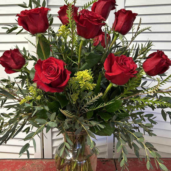 Red roses arranged in a clear glass vase with greenery and yellow filler flowers